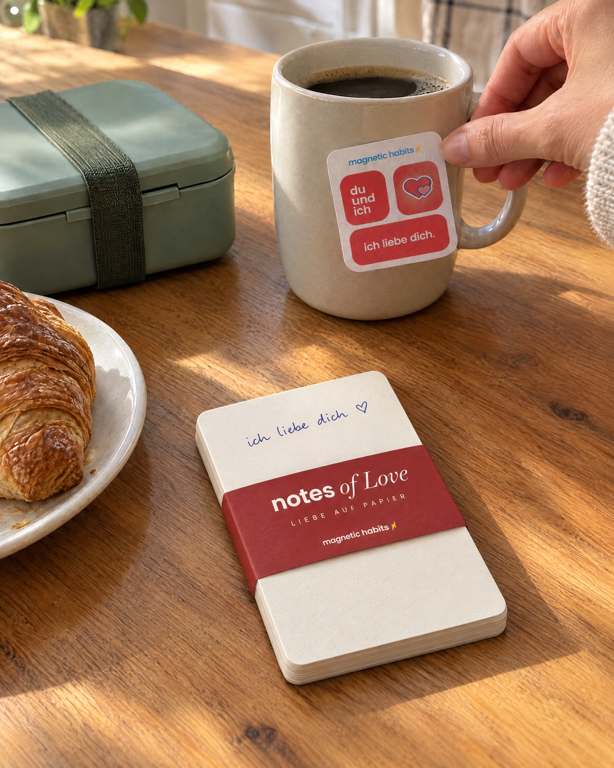 notes of Love: Notizblock mit roter Banderole am Frühstückstisch, daneben eine Note an der Kaffeetasse (Visualisierung)